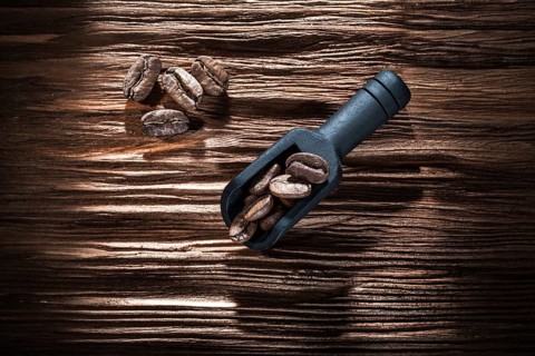 Black coffee seeds in scoop on vintage wooden board