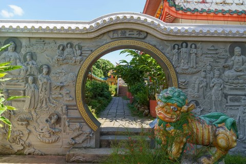 Entrance gate with stone reliefs and colourful figure. Leads to a well-kept garden path, penang,