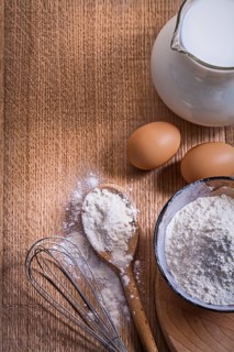 Aerial view copyspace composition pitcher with milk flour in bowl and spoon eggs corolla on wooden