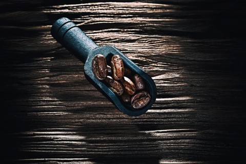 Black coffee grains in scoop on vintage wooden board