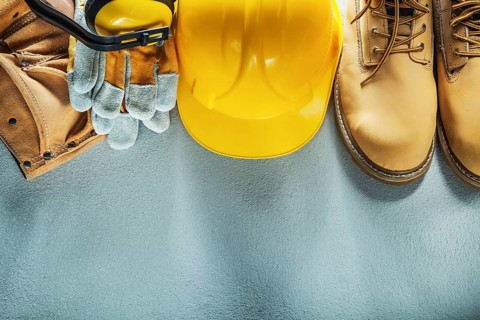 Building helmet tool belt safety gloves boots earmuffs on concrete background