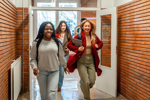 Happy multiethnic students running through a university hallway, celebrating friendship and