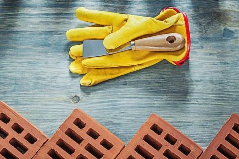Assortment of red construction bricks leather safety gloves palette knife building concept