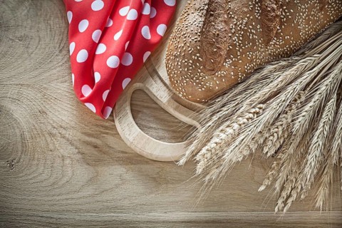 Bread chopping board wheat ears red tablecloth on wooden background