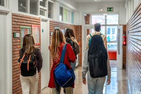 Diverse group of high school students walking together down a bustling school hallway, carrying