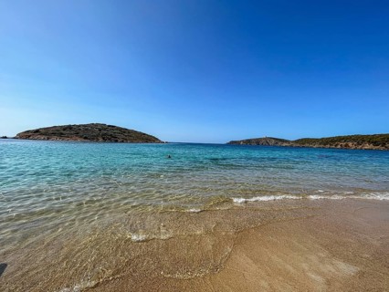 Calm beach with gentle waves and hills in the background under a blue sky, cagliari, sardinia,