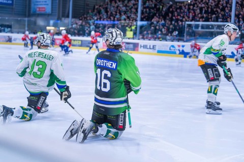 Two ice hockey players in green jerseys kneeling on the ice during a game in front of an audience,
