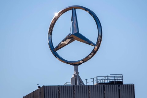 Large Mercedes-Benz logo on the roof of a modern building under a clear blue sky, star,
