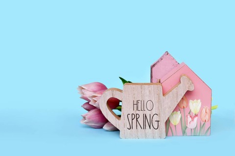Seasonal decor arrangement with house, pink tulip flowers and watering can with text 'Hello spring'