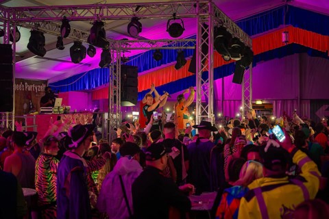 Zipfelbuben, people celebrating at a concert in a decorated tent with colourful lights, carnival,