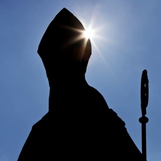 Anonymous Catholic bishop with mitre and crozier as a silhouette against the light, symbolic photo