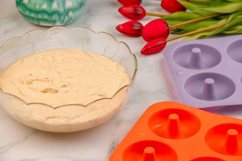 Dough placed next to baking moulds for donuts, red tulips in the background