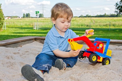 Three-year-old boy on the playground, sitting in the sandpit and playing with an excavator, toy,