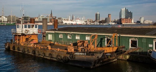 Hamburg harbour, working ship WASSERBAU I in front of wooden barracks, city skyline with museum