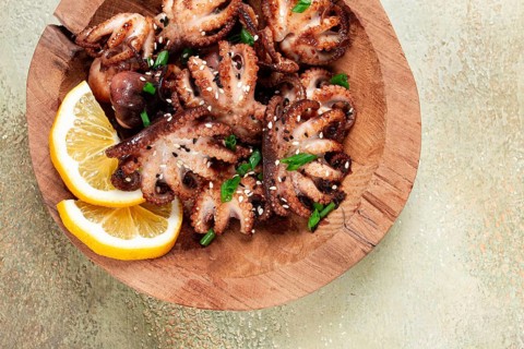 Grilled baby octopus with green onions, lemon slices, on a wooden plate, homemade, no people