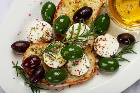 A plate with a snack, ciabatta bread with cheese and olives, olive oil, spices and herbs, top view,
