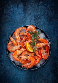 Freshly frozen shrimp on ice, with lemon and rosemary, on a dark blue table, top view, no people