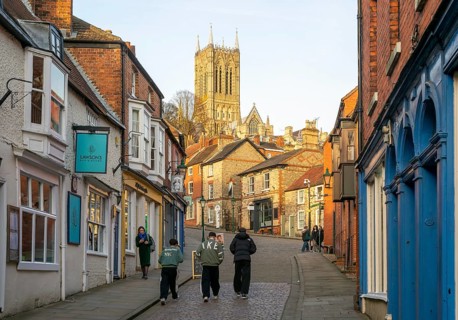 People walking up Steep Hill in evening light, cathedral tower rising above buildings, Lincoln,