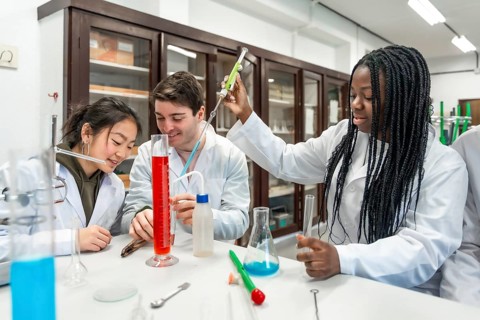 Multi ethnic university students wearing lab coats conducting a chemistry experiment using colorful