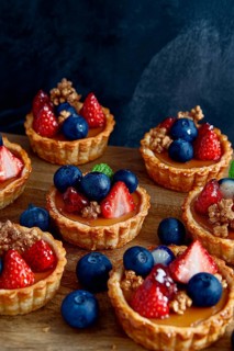 These miniature fruit tarts, adorned with fresh blueberries and vibrant strawberries, sit on a
