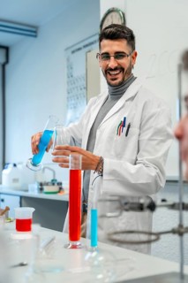 Young male scientist pouring blue liquid into laboratory glassware while smiling during an