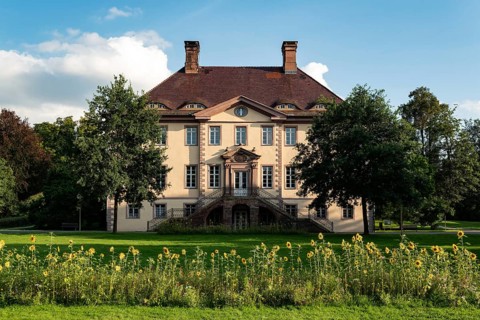 Schieder Castle presents itself under a blue sky as an elegant manor house with a flower meadow and