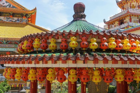 Richly decorated pavilion with hanging red and yellow lanterns. Temple in the background, penang,
