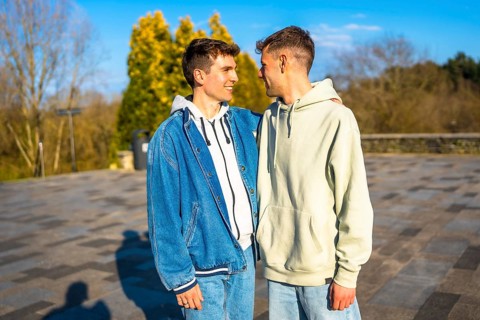 Two men embracing and smiling in a public park, sharing a joyful romantic moment together under the