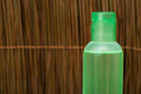 Green transparent cosmetic bottle. Wooden background