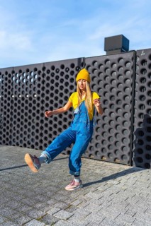 Urban dancer performing a street dance move outdoors, wearing a yellow beanie and blue denim