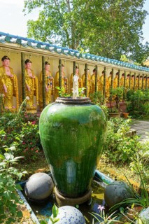 Garden with large ceramic pot, plants and Buddha figures along a wall, penang, malaysia