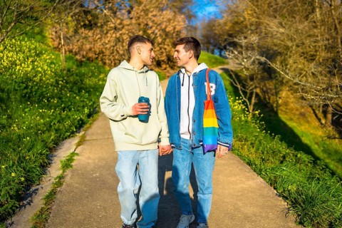 Young caucasian gay couple holding hands and walking in a park, enjoying a sunny day together