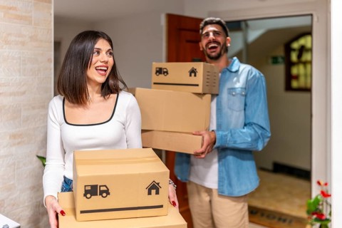 Cheerful homeowners carrying cardboard boxes, smiling as they enter their new apartment, embracing
