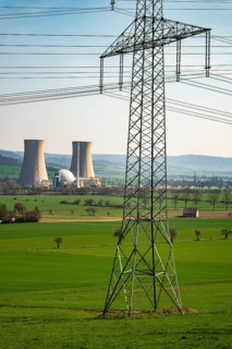 An electricity pylon stands in a green landscape with the Grohnde nuclear power plant in the