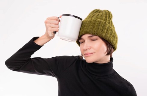 Funny girl in a green knitted hat put a white mug to her temple. The concept of a hangover after