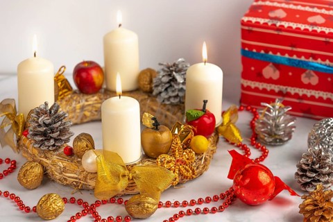 Advent wreath with four burning candles, red pearl necklace and Christmas decorations next to it