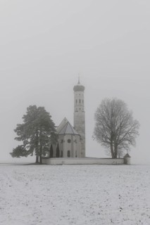 A gothic church with a tower in a foggy snowy landscape, pilgrimage church St. Coloman, near