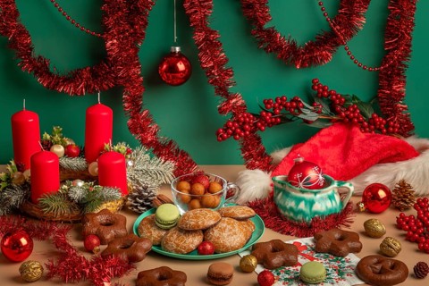 Table with Christmas decorations, biscuits and Advent wreath with red candles, framed by garlands