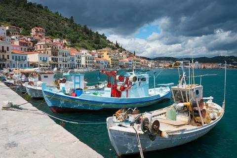 Boats moored at a pier of a coastal town under a slightly cloudy sky with green hills in the