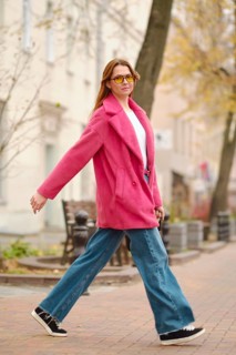 A person walks confidently along a tree-lined street, wearing a pink coat, sunglasses, and