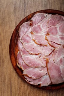 Sliced pork neck, boiled and smoked, smoked pork neck, sliced, on a wooden chopping board, close-up