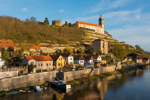 Idyllic town view with church on a hill by the river in the evening sun, surrounded by autumnal