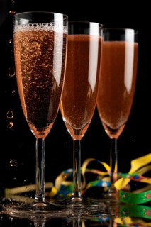 Three champagne glasses on a dark background, liquid bubbling, colourful ribbons next to them