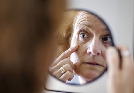 Symbolic photo on the subject of eye wrinkles. A woman looks at her eye wrinkles in the mirror.