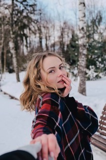 Curly blond pretty young woman in poncho in winter park. Cold weather. Holidays, season and leisure