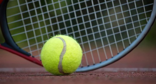 Close up of a yellow tennis ball and a tennis racket lying on a tennis hard court surface is