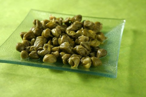 Capers with vinegar snack on a transparent plate, green background