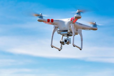 Flying quadcopter drone UAV with digital camera in blue sky, takes aerial pictures world around
