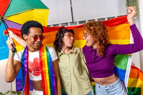 Non binary and transgender people dancing waving rainbow lgbt flag celebrating a party at home