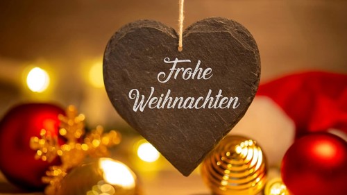 Christmas greetings: Heart with the inscription FROHE WEIHNAHCHTEN in front of Christmas